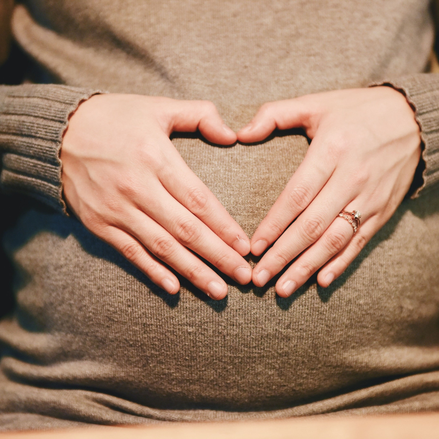 Pregnant belly being embraced by heart-shaped hands